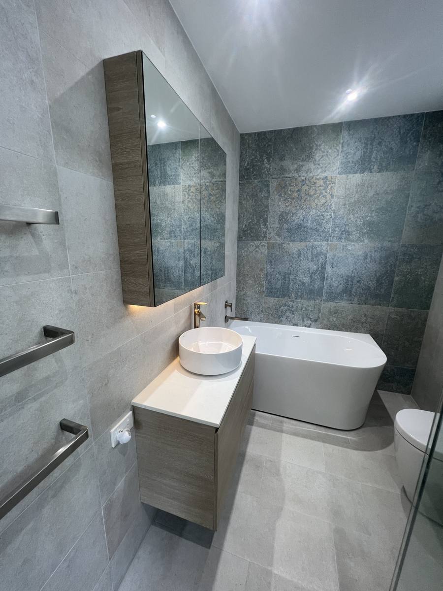 A finished bathroom with grey tiling and a glass shower screen