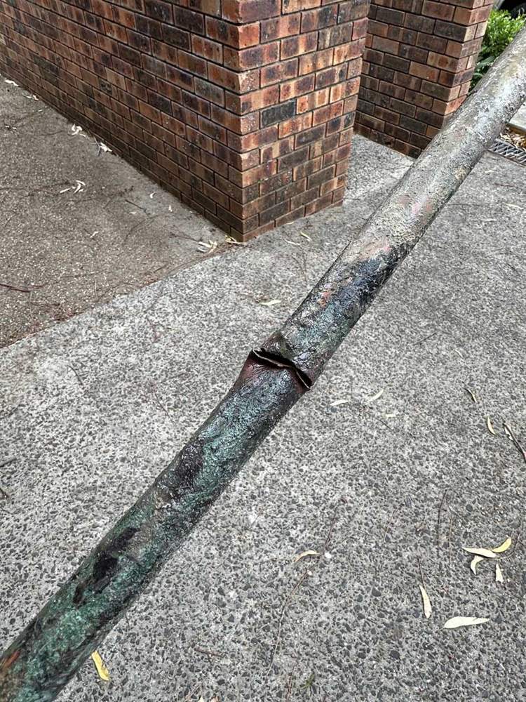 A split galvanised water pipe lifted out of a driveway