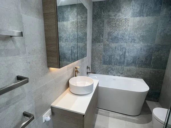 Finished bathroom renovation with grey tiles, a basin and a freestanding bath