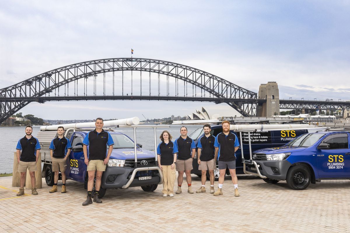 The STS Plumbing team standing with three signwritten utes at Sydney Harbour